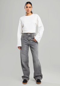 Top blanco de manga larga combinado con jeans de tiro alto de pierna ancha en gris. Zapatillas negras con suela marrón completan el atuendo. Diseño sencillo y estilo casual.