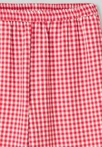 Tissu à carreaux rouge et blanc avec une taille élastique, présentant une texture légère et des détails froncés le long du bord supérieur.