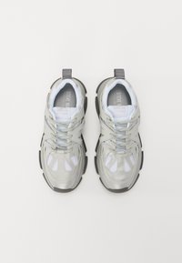 Zapatillas plateadas metálicas con detalles de malla, punta redondeada, suela de goma gris y cordones prominentes. Presenta una lengüeta en la parte posterior.