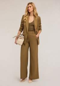 Hnědý na míru šitý blejzr přes ribbed hnědý top, k tomu odpovídající široké kalhoty a béžová kabelka. Světle růžové špičaté lodičky. Hladké textury.