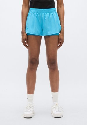 Hele sinised spordipüksid elastse vöökohaga, valmistatud sileda kangaga. Kandes tumelõhnavate lühikeste pükste kohal, külje peal lõhikud. Valged spordijalatsid ja sokid.