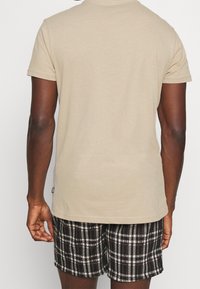 Beige cotton t-shirt with short sleeves, paired with black and white checkered shorts featuring a relaxed fit and elastic waistband.