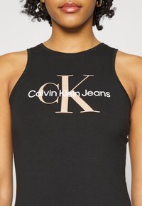 Svart bomullstopp utan ärmar med en djärv, ljusrosa grafik "CK" och texten "Calvin Klein Jeans" på framsidan, med en åtsittande design.