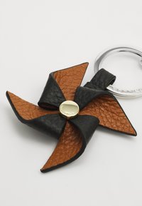 Accesoriu din piele sub formă de moară de vânt, având piele texturată neagră și maro, cu un accent din metal de culoare aurie în centru.