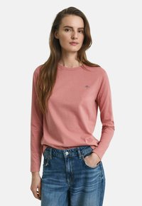 Langärmliges, pinkes T-Shirt aus weicher Baumwolle mit rundem Ausschnitt und kleinem Logodetail. Trägt man zu blauen, hochgeschnittenen Jeans.