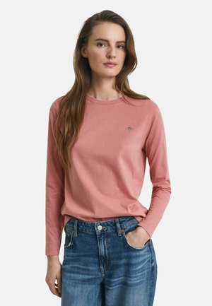 Long-sleeve, pink T-shirt in soft cotton with a round neckline and small logo detail. Worn with blue, high-waisted denim jeans.