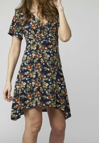 Blommig klänning med marinblå bakgrund, korta ärmar och V-ringning. Har en skräddarsydd midja och en något längre bakdel.
