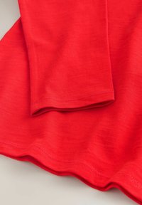 Tissu rouge avec des coutures visibles et des bords repliés sur une surface plane, montrant la texture et les détails de l'ourlet.