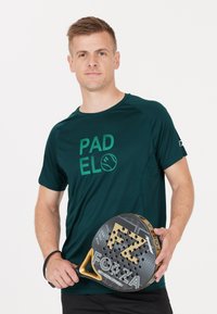 Mörkgrön sporttröja med "PADEL"-grafik, som bärs av en person som håller ett svart och guld padelracket med mönstrad yta och logotyp.