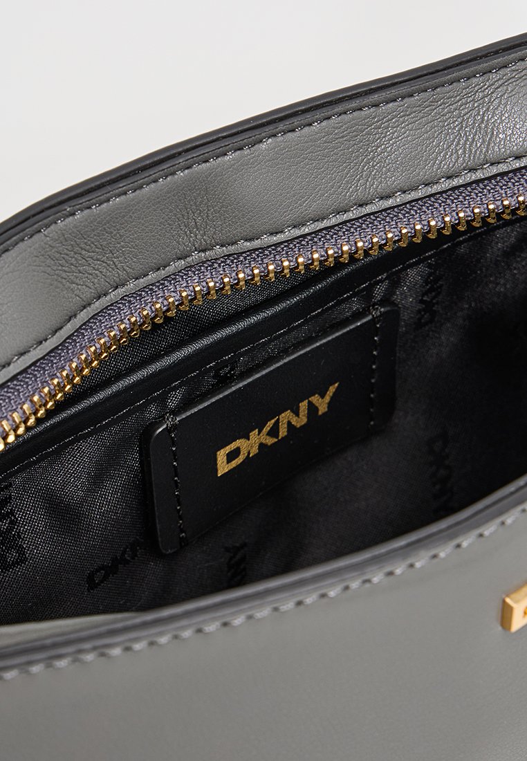 Graues Lederhandtaschen-Innenleben mit einem goldenen Reißverschluss, DKNY-Logotag und einem glatten Textilfutter mit einem subtilen Logomuster.