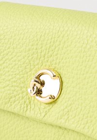 Lähikuva vaaleanvihreästä, strukturoidusta nahasta, jossa on kiiltävä kultainen pyöreä solki, jossa on toisiinsa kietoutuva silmukkakuvio.