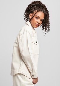 Lichtbeige denimjack met een relaxte pasvorm, enkele borstzak en knoopsluiting. Heeft lange mouwen en een gladde textuur.