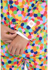 Abito a pois colorati con cerchi luminosi in rosso, blu, verde, giallo e rosa. I dettagli includono bottoni blu e cuciture a contrasto.