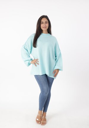 Lichtblauwe oversized trui met een hoge hals en losse mouwen, gecombineerd met strakke blauwe jeans en transparante hakken.