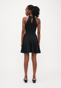 Robe noire à dos nu avec un corsage ajusté, une jupe évasée et un détail en trou de serrure au dos. Tissu texturé avec une finition lisse.