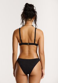 Črni bikini komplet z teksturiranim vzorcem. Ima nastavljive naramnice in zlato-tonirano okovje, kar ponuja minimalističen in sodoben dizajn.
