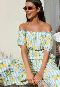 Vestido off-the-shoulder con un patrón de rayas azules y blancas, decorado con limones amarillos y hojas verdes. Tejido suave con mangas fruncidas.