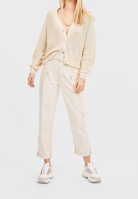 Cardigan beige clair en maille avec boutons, associé à un pantalon taille haute de couleur crème et des baskets blanches épaisses. Design simple.