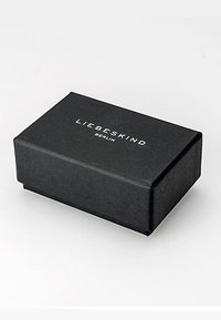 Scatola nera con texture, di forma rettangolare, con il logo "LIEBESKIND BERLIN" in rilievo sulla parte superiore, design minimalista con bordi eleganti.