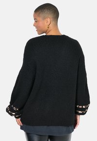 Černý oversized svetr s texturovaným pletením, zdobený leopardím potiskem na manžetách. Klasický design s kulatým výstřihem.