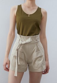 Olijfgroen mouwloze top met een ronde accent, gecombineerd met hoge beige shorts met een gestrikt ceintuur en twee voorkruiszakken.