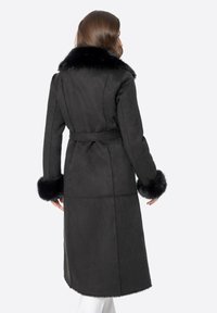 Abrigo largo de ante negro con cuello y puños de piel sintética, ceñido en la cintura, con un corte recto y textura suave.