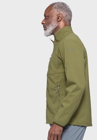 Olive green softshell jacket with high collar, zippered front and side pockets, and elastic cuffs. Features brand logo on the shoulder.