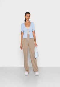 Cardigan de manga curta em azul claro com fecho de laço, top de tanque bege, calças largas bege e sapatilhas rosa pálido. Bolsa azul clara.