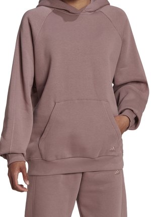 Person wearing mauve Adidas hoodie and matching sweatpants, with hand in hoodie pocket, cropped at neck and thighs.