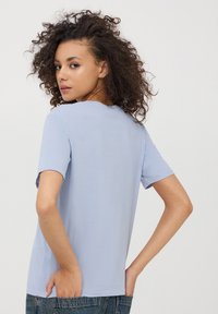 Jasnoniebieska bawełniana koszulka z krótkim rękawem, okrągłym dekoltem, luźnym krojem i gładką fakturą, widziana z tyłu.