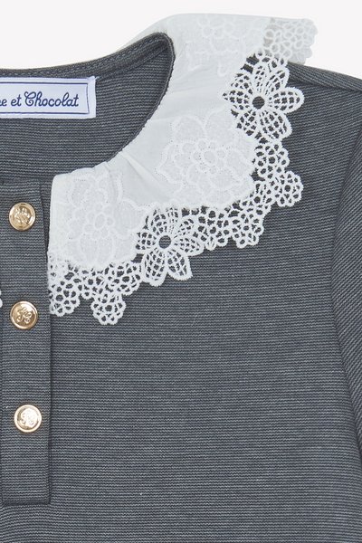 Haut gris avec un col en dentelle blanche agrémenté de motifs floraux, trois boutons dorés sur le côté gauche, et une surface en tissu texturé.