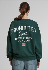 Zelená mikina s bielym textom "ZAKÁZANÉ" a grafickými nožnicami. Obsahuje text "SAVILE ROW LONDÝN" a malú vlajku Spojeného kráľovstva na spodnej časti.
