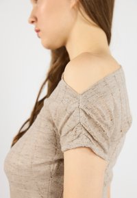 Beige stickad topp med korta, samlade ärmar och en off-the-shoulder design, med en texturerad tyg och subtilt mönster.