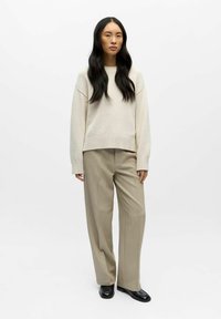 Beige strikket genser med løs passform, ribbestrikket hem, kombinert med lyse beige skreddersydde bukser og svarte loafers. Glatt tekstur gjennom hele.