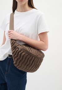 Borsa a spalla marrone trapuntata con forma arrotondata, realizzata in materiale imbottito, dotata di una cerniera e di una ampia tracolla.
