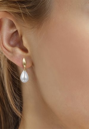 Kvindeøre med en gylden ørering med en stor dråbeformet perle hængende under øreflippen.