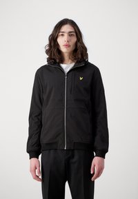 Jachetă neagră cu fermoar, cu glugă, având un accent de logo galben, buzunare frontale și manșete ribbed. Textură netedă și design casual.
