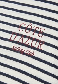 White fabric with horizontal navy blue stripes featuring red text "CÔTE D'AZUR Sailing Club" printed on it.