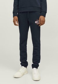 Mørkeblå bomulds-joggingbukser med elastisk talje, tapered ben og sidelommer; har et farverigt logo på låret. Paireret med hvide sneakers.