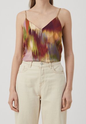 Mujer que lleva un top sin mangas con tirantes finos y estampado abstracto multicolor, metido dentro de unos pantalones crema de talle alto.