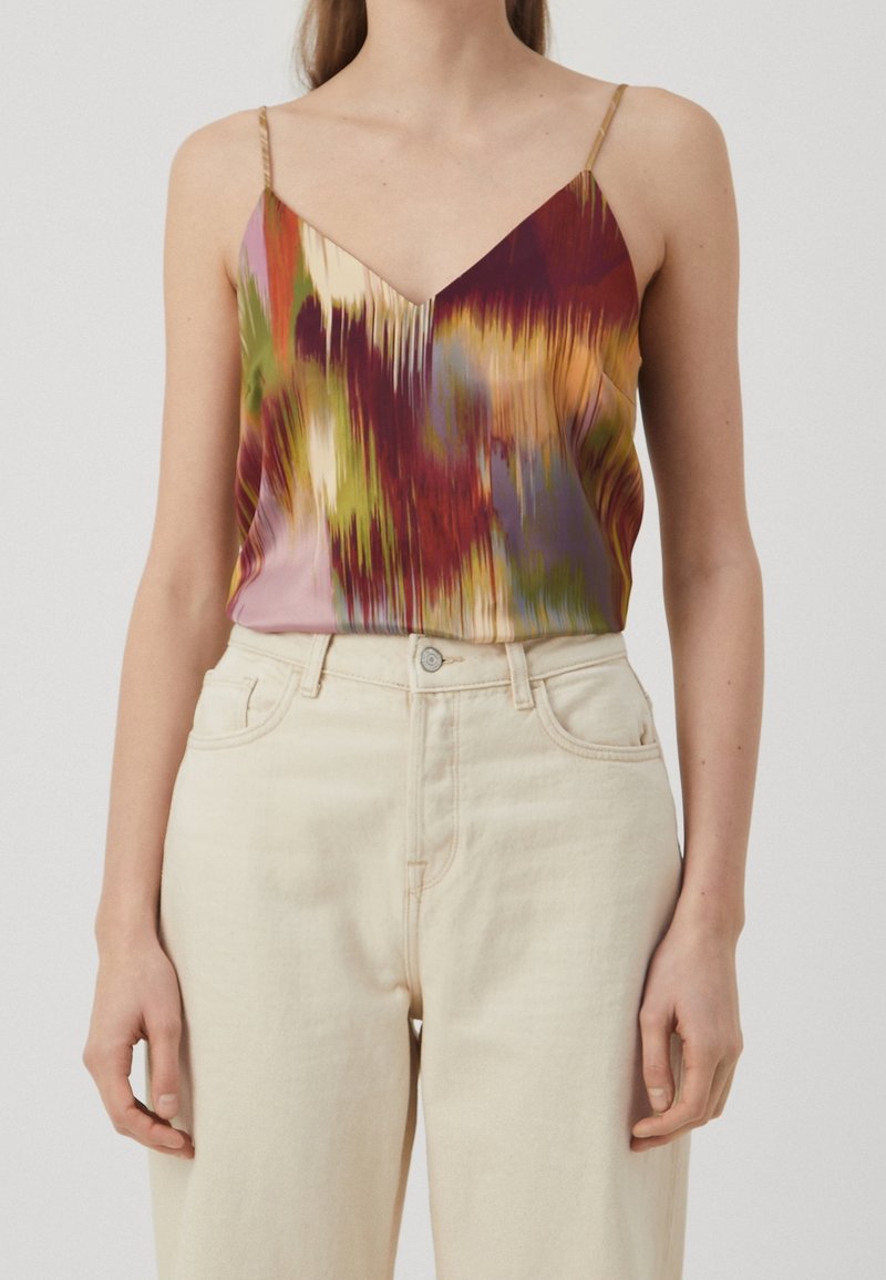 Femme portant un haut sans manches à fines bretelles avec un imprimé abstrait multicolore, rentré dans un pantalon crème taille haute.