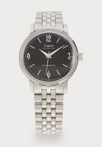 Montre automatique en acier inoxydable argenté avec un cadran noir, des chiffres arabes et un bracelet à maillons. Elle dispose d'une lunette polie et de fines aiguilles.