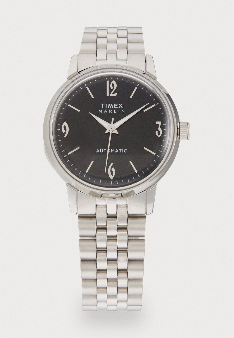 Montre automatique en acier inoxydable argenté avec un cadran noir, des chiffres arabes et un bracelet à maillons. Elle dispose d'une lunette polie et de fines aiguilles.