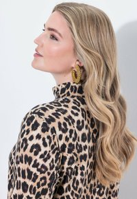 Bluzka w panterkę z wysokim kołnierzem; długie, falowane blond włosy; duże złote kolczyki-koła zdobione małymi koralikami.