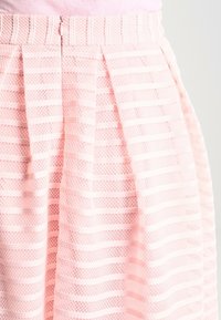 Falda de color rosa claro con franjas horizontales texturizadas, plisados y una cintura elástica con una cremallera trasera visible.