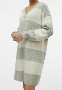 Robe pull tricotée avec col en V, manches longues et coupe ample, présentant des rayures horizontales alternées gris et crème. Texture douce.