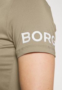 Camiseta de manga corta color caqui con un logo en relieve blanco "BORG" en la manga izquierda, hecha de una tela suave y elástica.