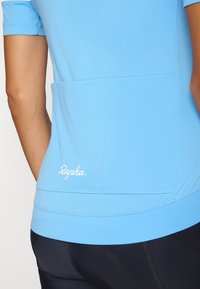 Jasnoniebieska, krótko rękawowa koszulka rowerowa z kieszenią z tyłu i białym logo "Rapha". Gładki, elastyczny materiał z dopasowanym krojem.
