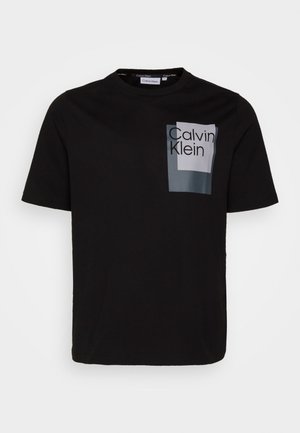 T-shirt en coton noir avec une poche avant imprimée du logo "Calvin Klein" en blanc et gris, col rond et manches courtes.