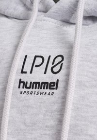 Gros plan sur le tissu d'un sweat à capuche gris clair avec le logo noir "LPLØ hummel SPORTSWEAR" et des cordons blancs.